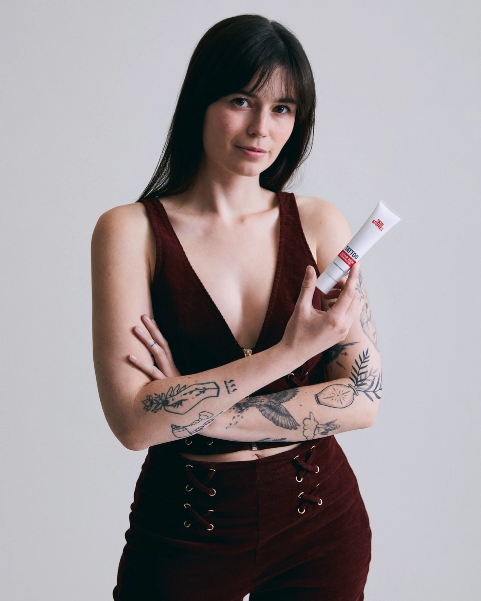 Frau mit Tattoos hält Tattoo-Creme in der Hand, blickt in die Kamera