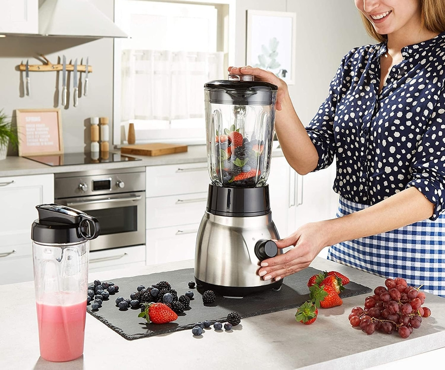 Frau mit Mixer, Früchten und Smoothie in der Küche.