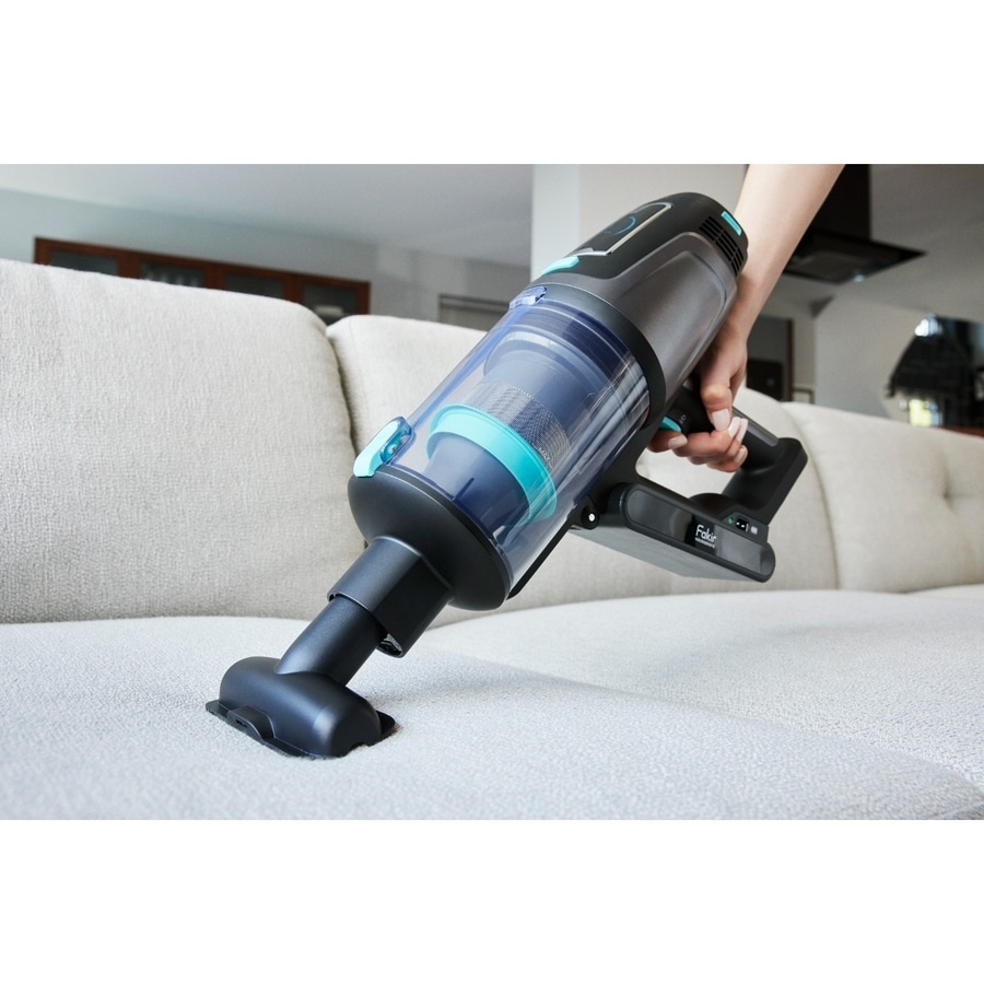 A person is vacuuming a white sofa with a handheld vacuum cleaner.