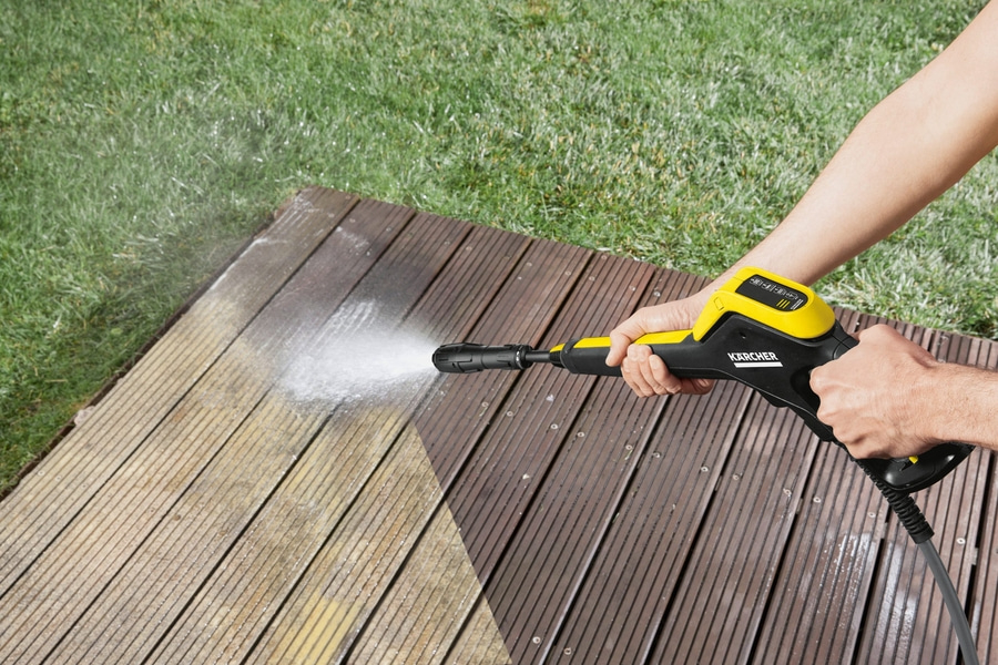 Person reinigt Holzterrasse mit Hochdruckreiniger, Wasserstrahl, Garten, sauber