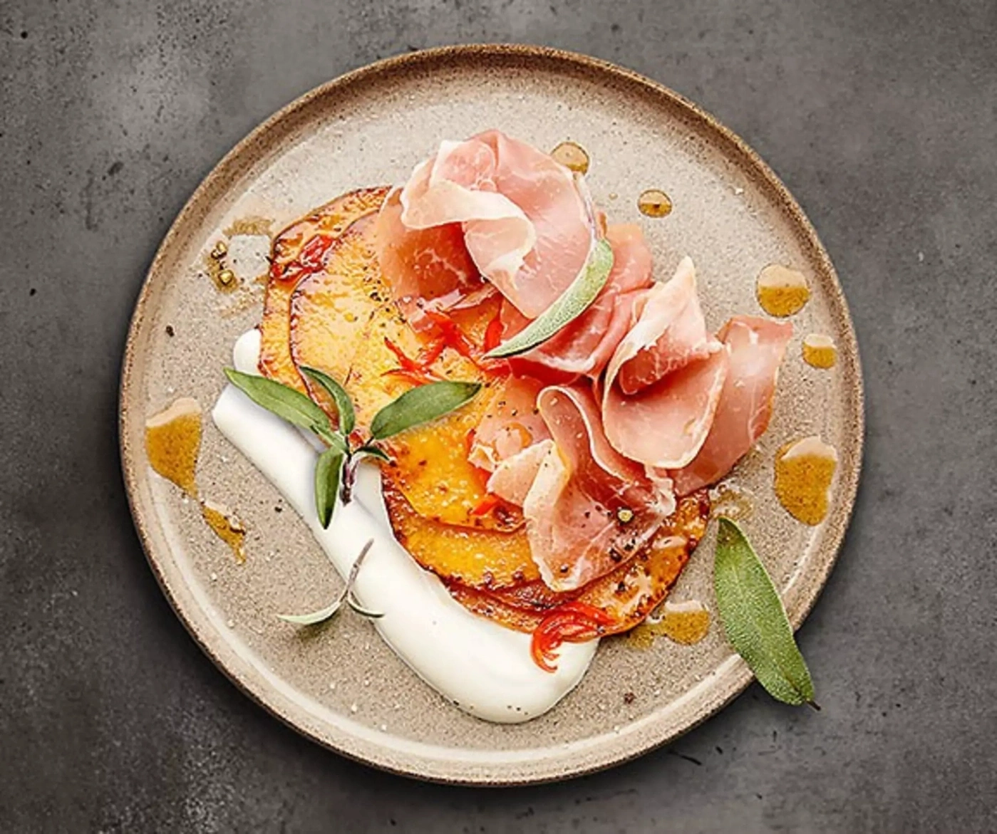 Gegrillte Süßkartoffelscheiben mit Prosciutto und weißer Sauce auf einem Teller.