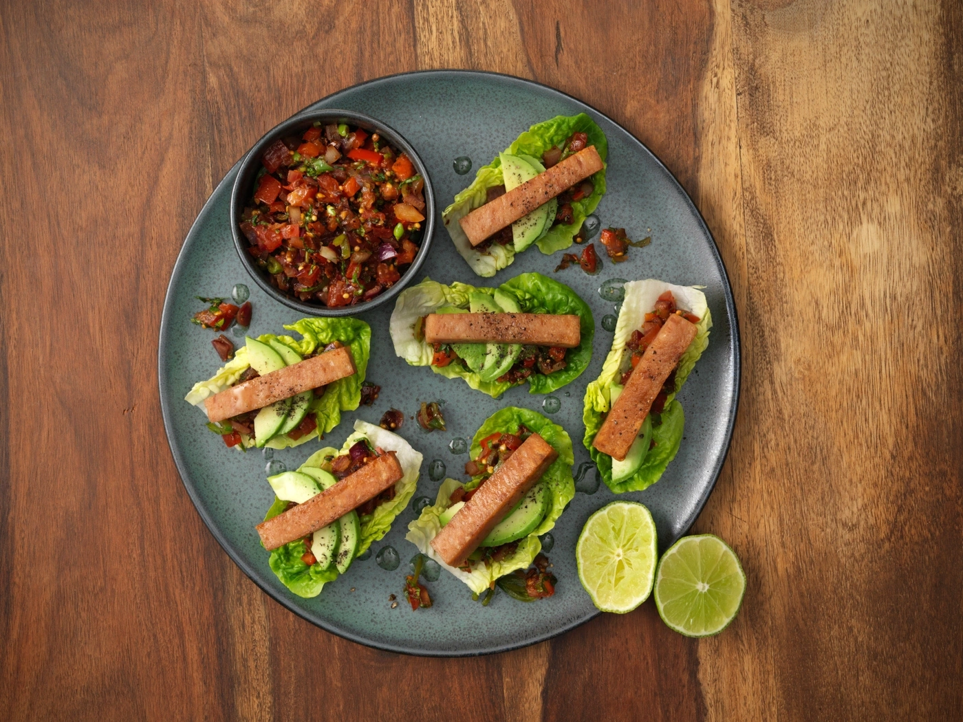 Schwein-Speck-Salat-Wraps mit Avocado und Salsa, serviert auf einem Teller mit Limettenspalten