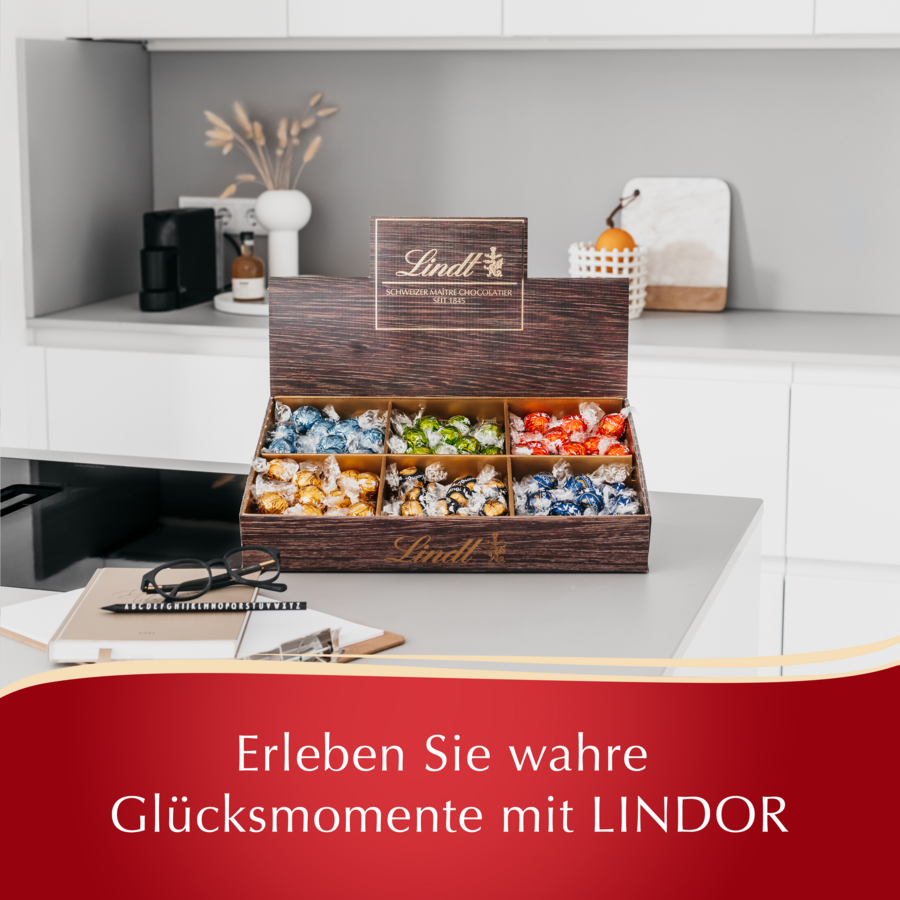 Eine Lindt Schachtel mit Pralinen auf einem Küchentresen mit einem Buch und Brille daneben.