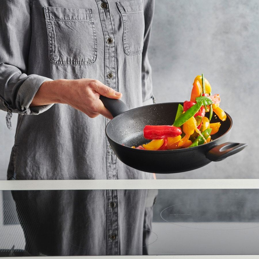 Person hält Pfanne mit Gemüse, kocht Essen, graues Hemd, Nahaufnahme, Küche