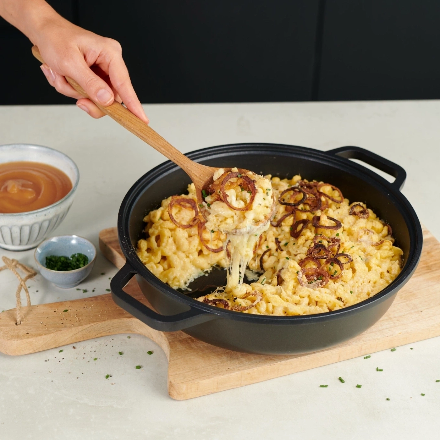 Käsespätzle mit Röstzwiebeln in einer Pfanne, serviert mit Soße und Kräutern