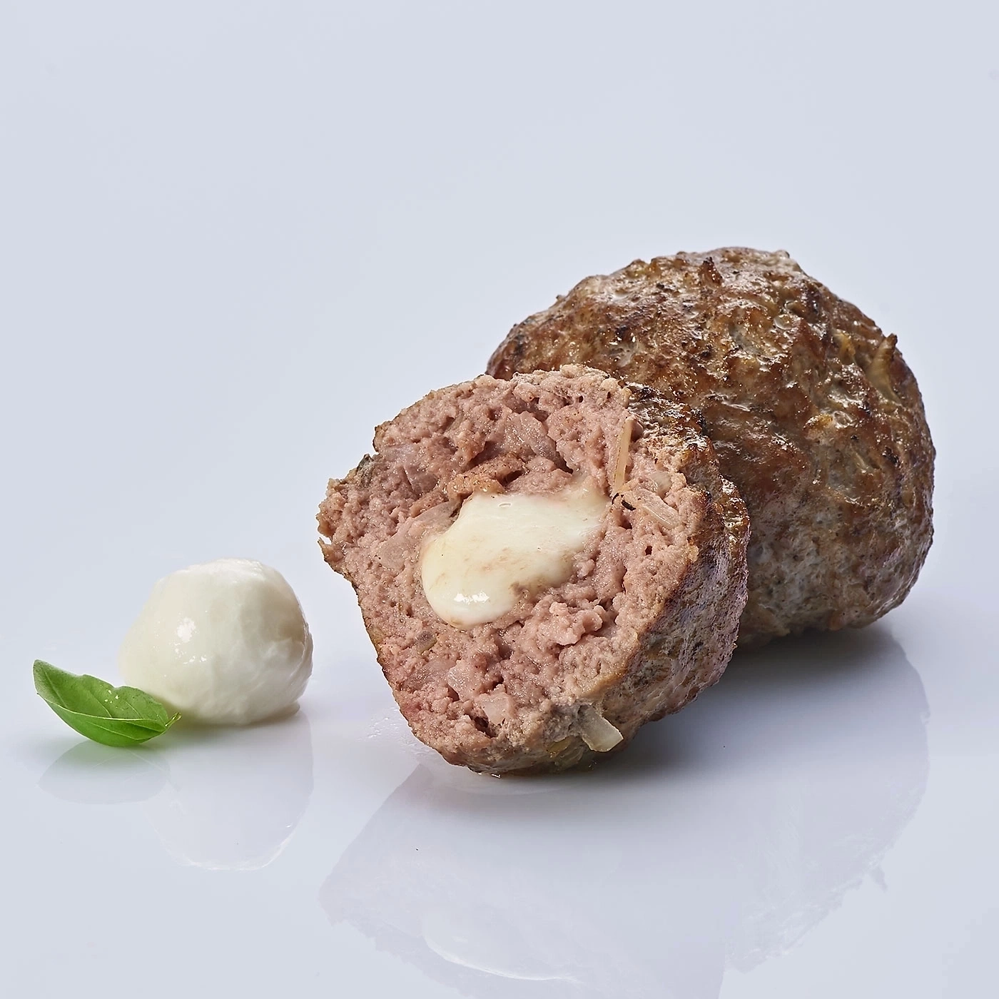 Fleischbällchen mit Käse gefüllt, Basilikum, Mozzarella, auf weißem Hintergrund