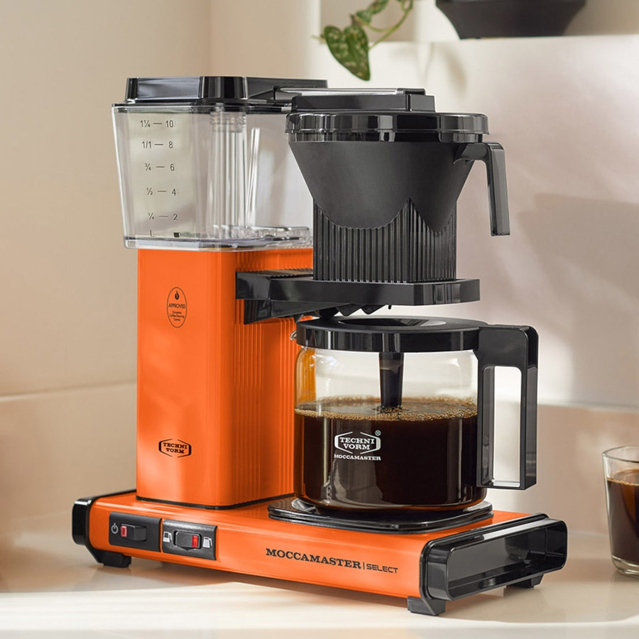 Orange Kaffeemaschine mit Glaskanne, Filter und Bedienfeld mit der Aufschrift MOCCAMASTER SELECT.