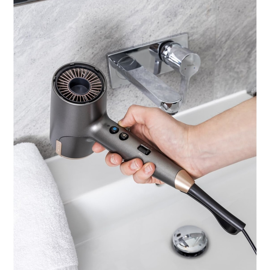Ein Mann hält einen dunklen Haartrockner über einem weißen Waschbecken.