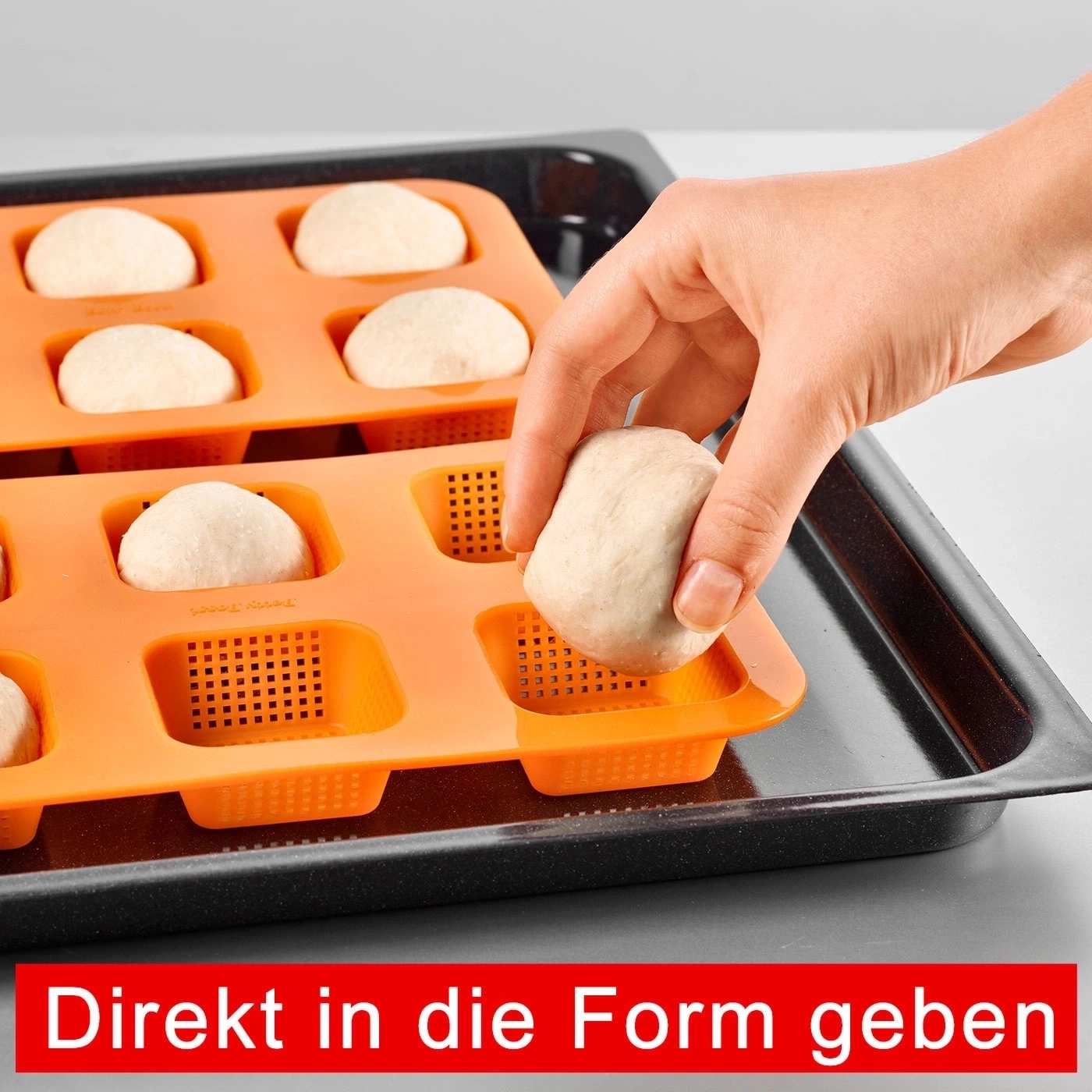 Hand legt Teig in orangefarbene Backform auf schwarzem Backblech. Direkt in die Form geben.