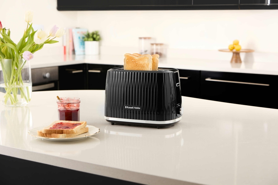 Schwarzer Toaster mit Toastbrot auf einer Küchenarbeitsplatte mit Blumen und Marmelade