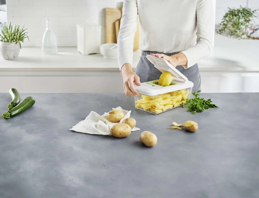 Person schneidet Kartoffeln mit einem Küchengerät auf einer grauen Arbeitsplatte.