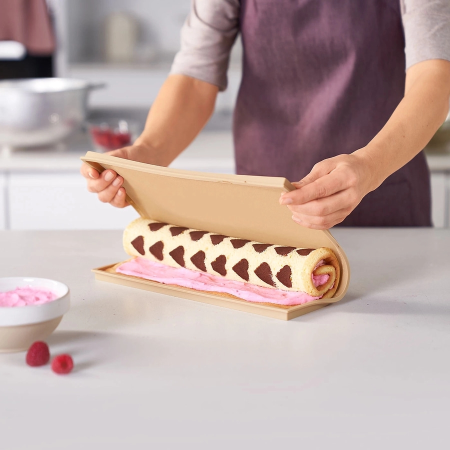 Person rollt Biskuitrolle mit Herzmuster aus der Form, Nahaufnahme