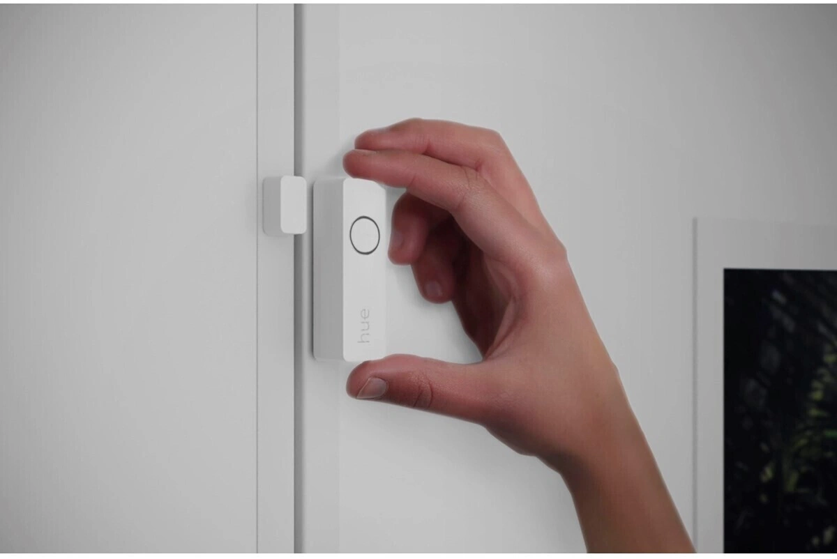 Ein Weißer Türkontaktsensor mit dem Hue-Logo wird an einer weißen Tür befestigt.