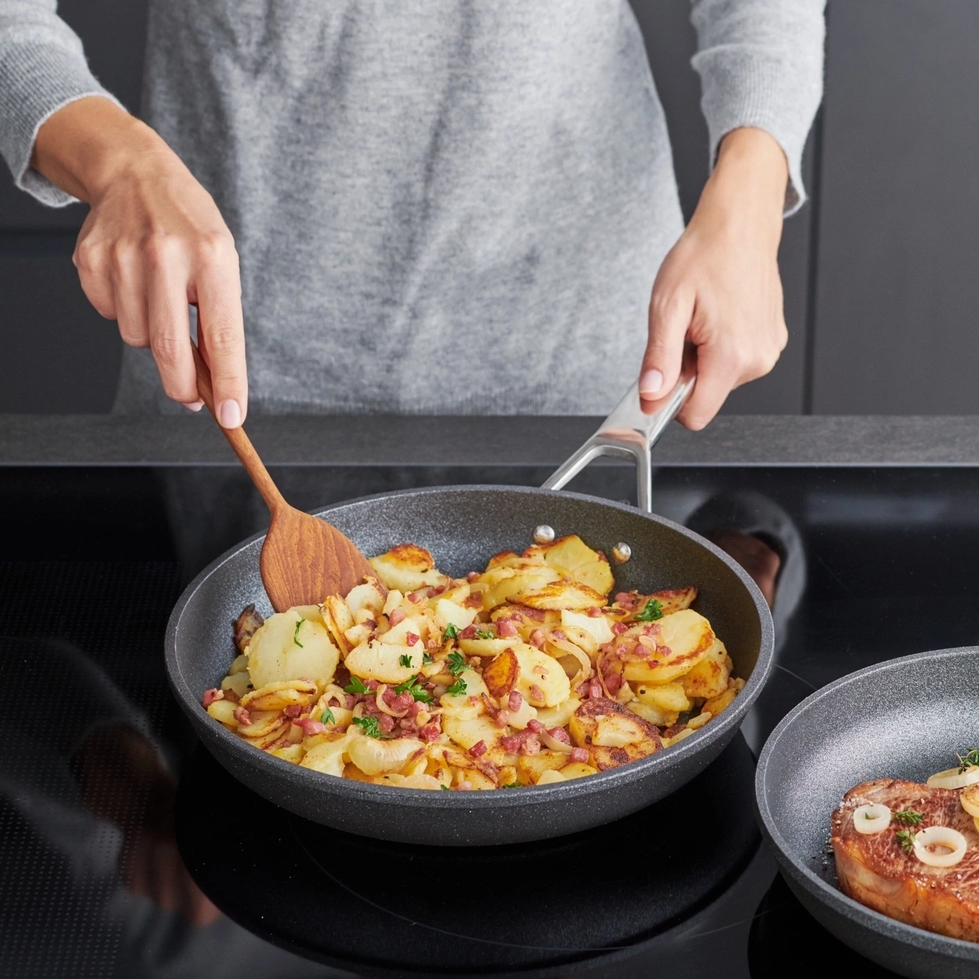 Person kocht Bratkartoffeln in einer Pfanne, hält einen Kochlöffel