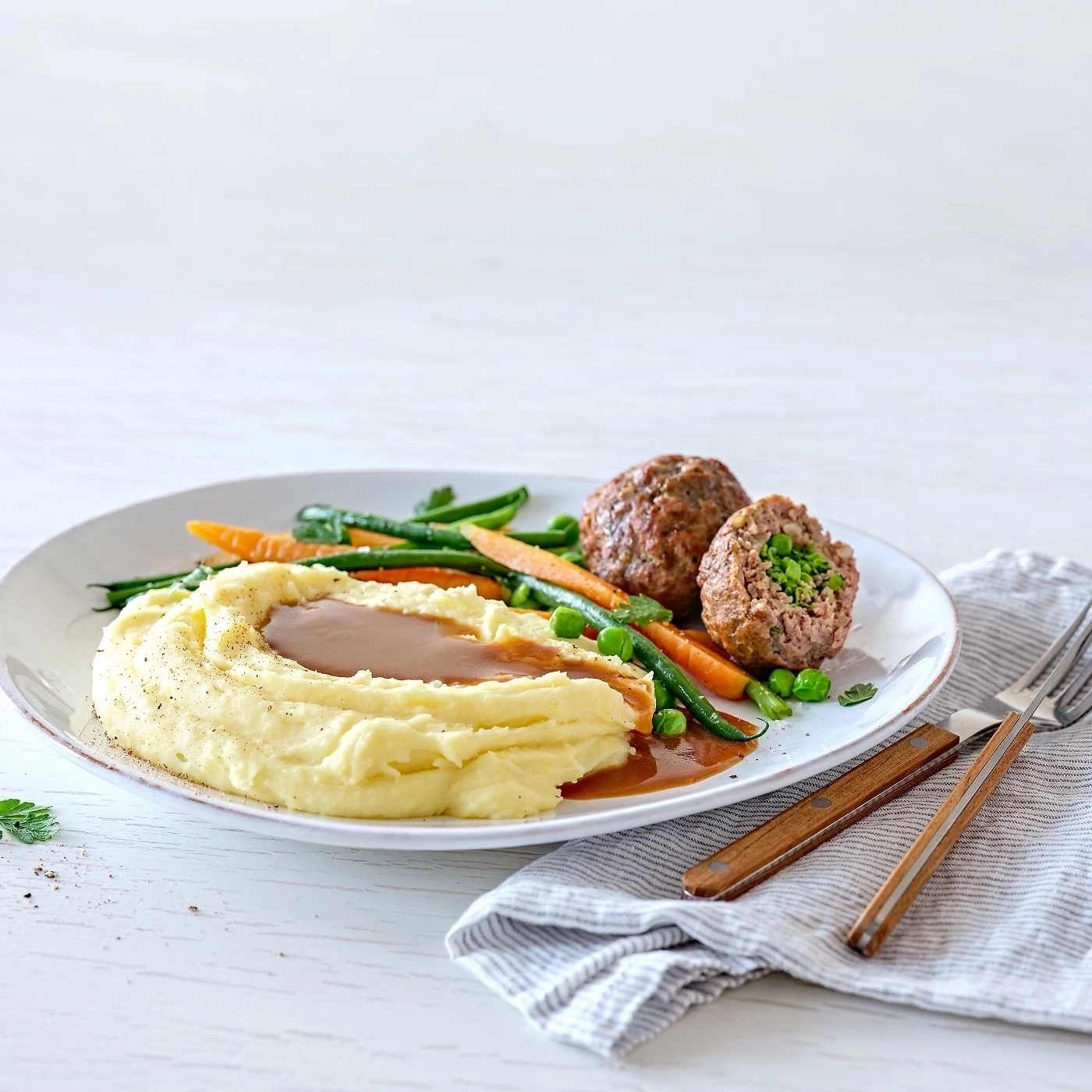 Teller mit Fleischbällchen, Kartoffelpüree und Gemüse, serviert mit Soße
