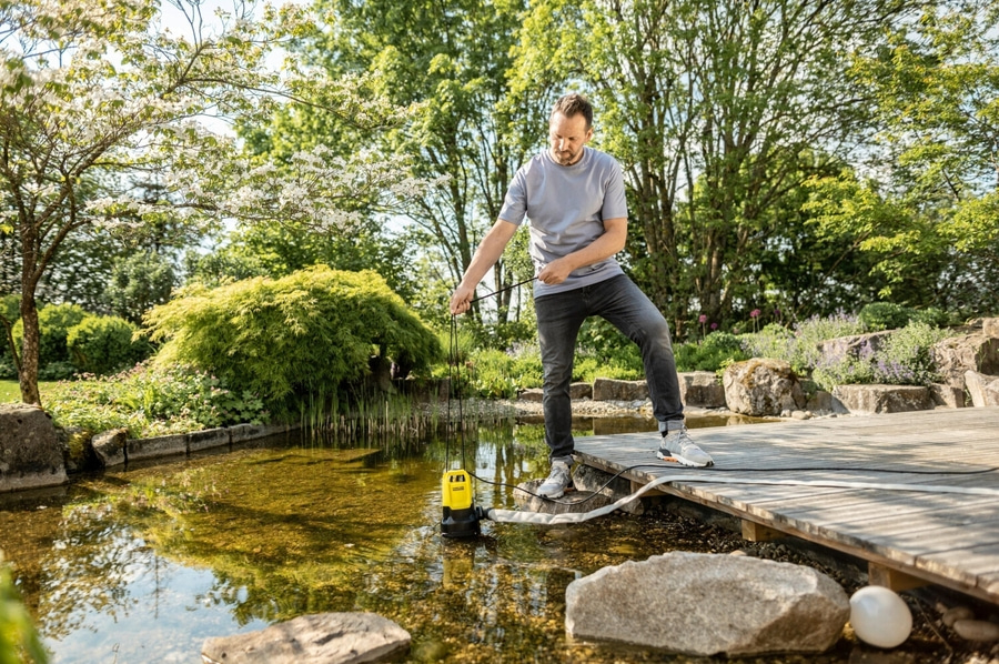 Mann mit Pumpe am Teich, umgeben von Natur und Bäumen