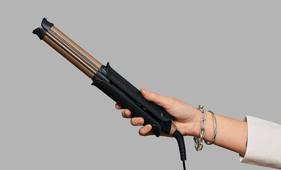 Person hält ein schwarzes und goldenes Glätteisen mit Armband