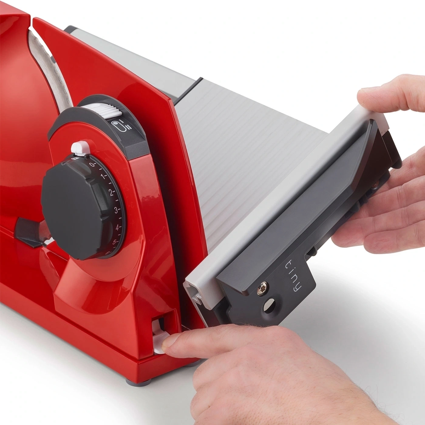 Eine rote Aufschnittmaschine mit einem Finger, der einen weißen Knopf drückt.