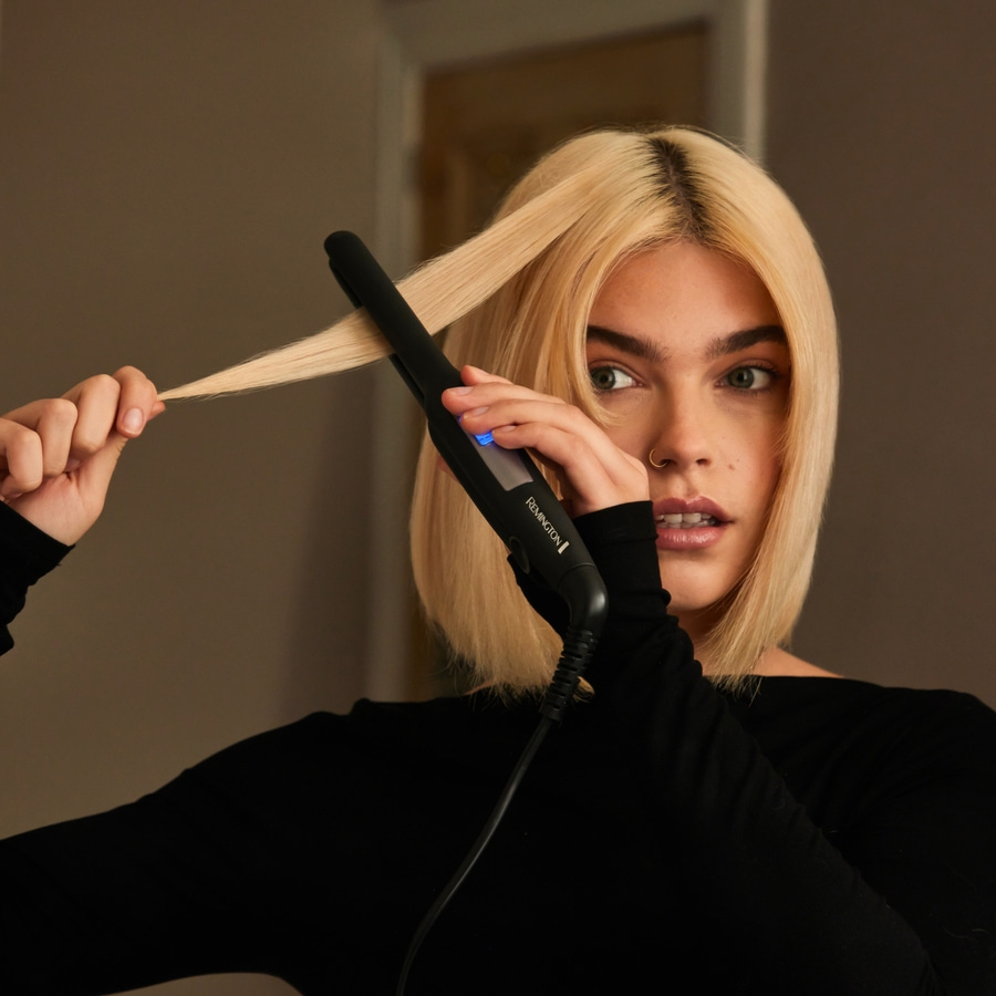 Eine Frau glättet ihr blondes Haar mit einem Glätteisen, Nahaufnahme.