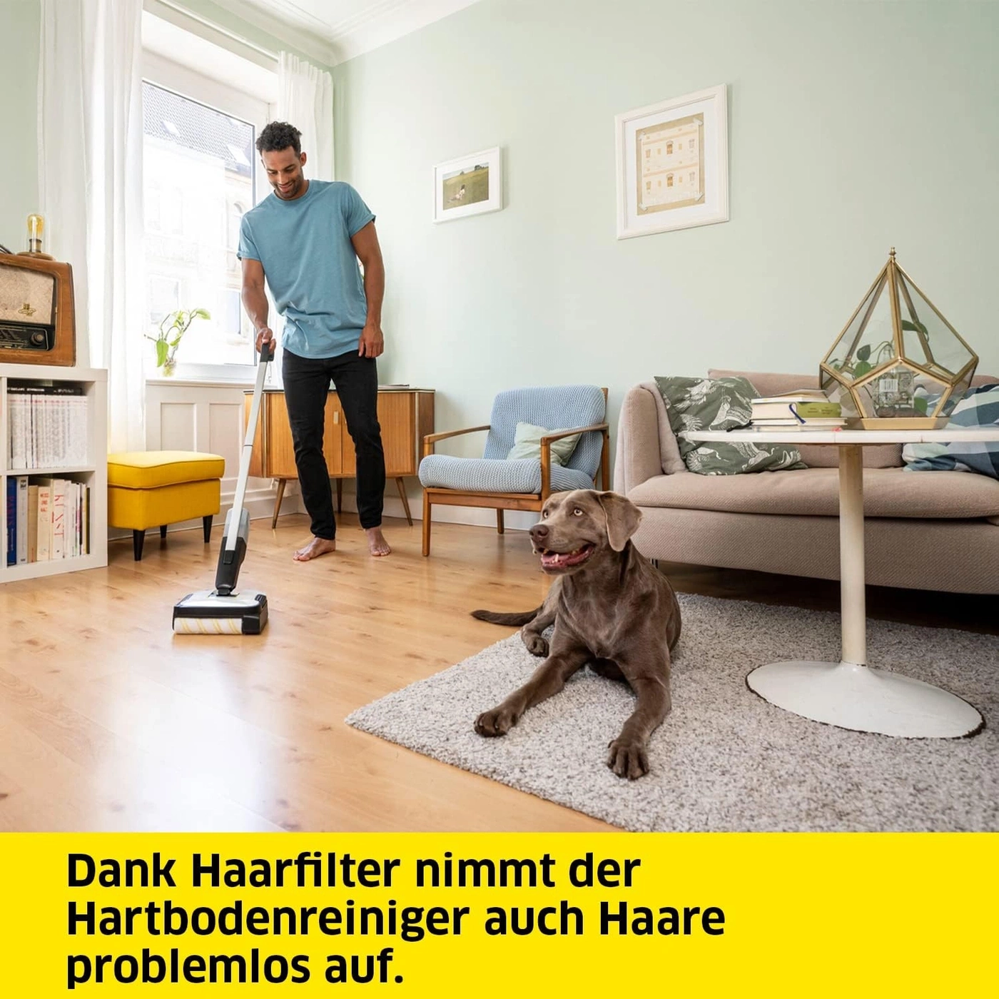 Mann saugt mit Bodenreiniger auf dem Holzboden, Hund liegt daneben.