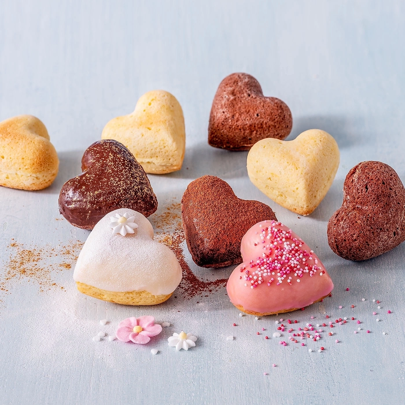 Herzförmige Gebäckstücke, dekoriert mit Zuckerstreuseln und Blumen, auf blauem Untergrund.