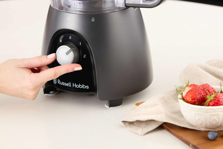 Nahaufnahme eines Mixers mit einer Hand, die den Knopf dreht, und Erdbeeren