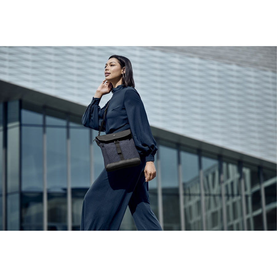 Eine Frau in einem blauen Outfit mit einer Umhängetasche geht vor einem Gebäude entlang.