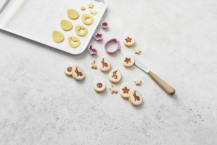 Osterkekse mit Ausstechern, Puderzucker und Marmelade auf hellem Hintergrund