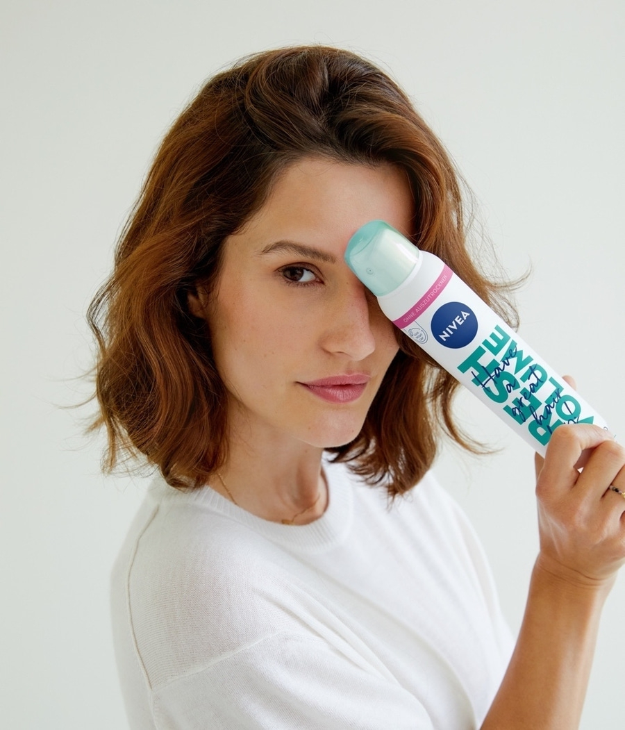 Frau hält Nivea-Produkt vor ihrem Gesicht, Blick in die Kamera, weißes Shirt