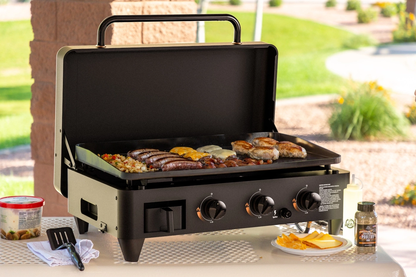Ein Griddle mit Würstchen, Burgern und Käse, draußen auf einem Tisch.