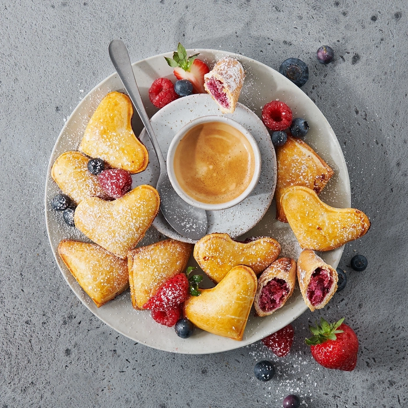 Teller mit Gebäck, Kaffee und Beeren, auf grauem Hintergrund