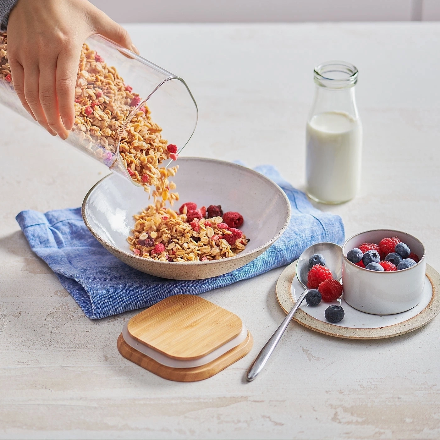 Müsli wird in eine Schüssel gegossen, daneben Beeren und Milch.