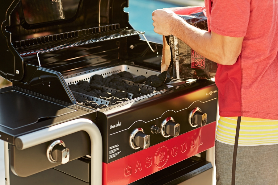 Person befüllt einen Gas-Kohle-Grill mit Holzkohle. Nahaufnahme.