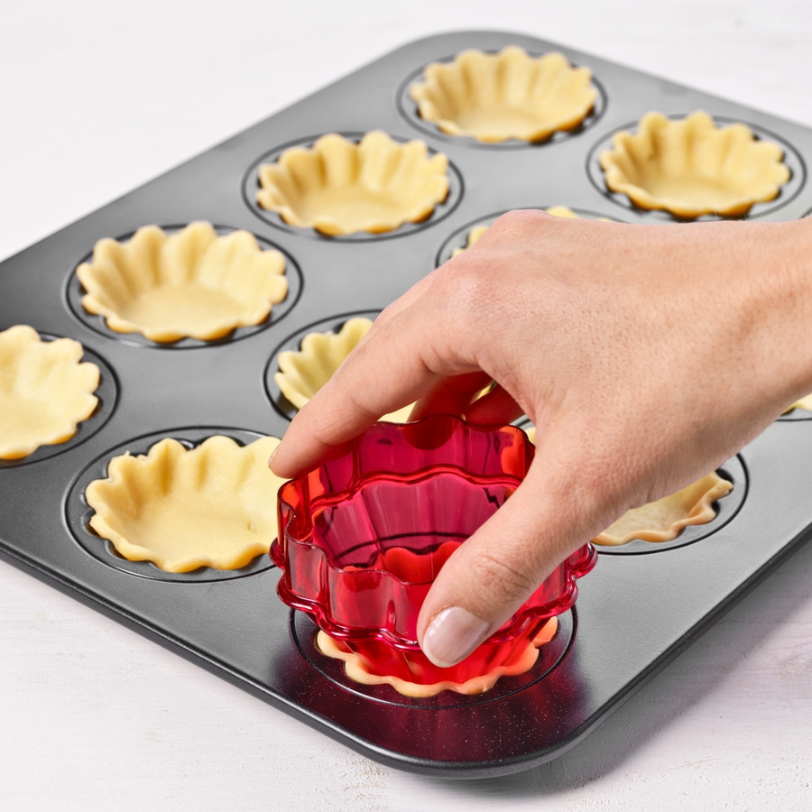 Hand formt Teig in Backform mit rotem Ausstecher für Mini-Tartelettes.