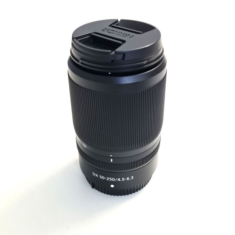 Ein schwarzes NIKON DX 50-250mm Objektiv mit Objektivdeckel.