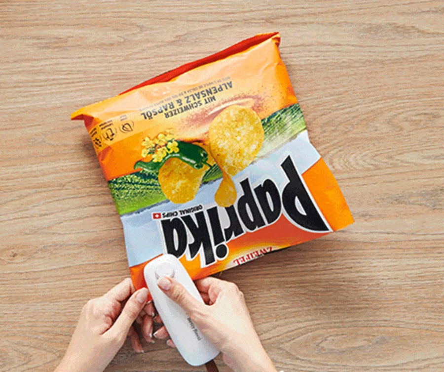 Eine Person, die eine Tüte Paprika-Chips mit einem weißen Gerät verschließt.