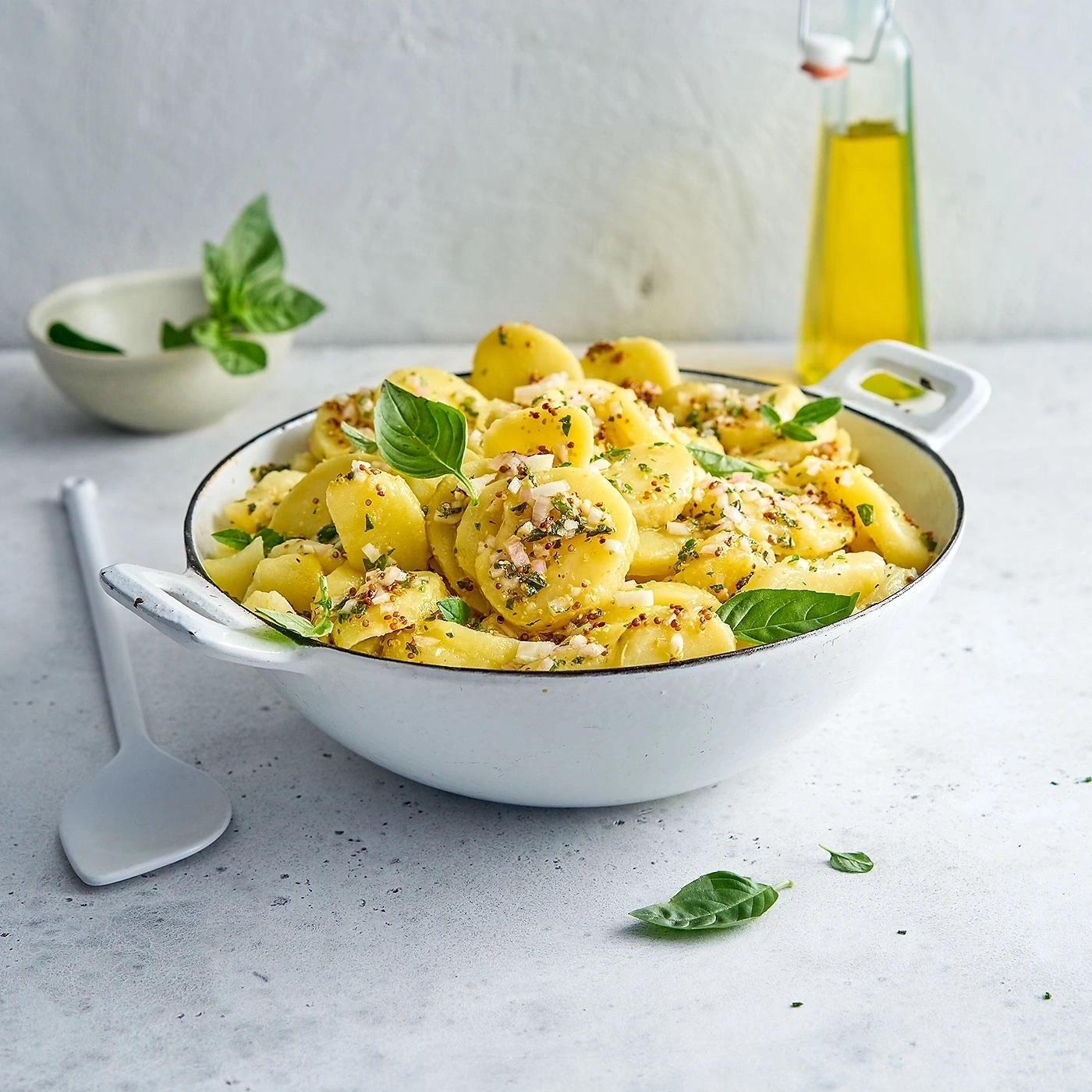 Kartoffelsalat mit Basilikum in einer weißen Schüssel mit Ölflasche