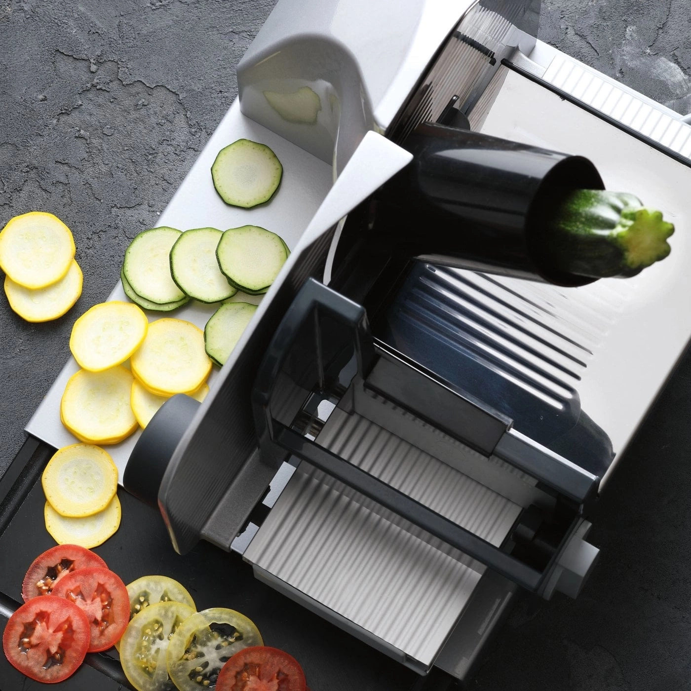 Ein Mandoline-Schneider mit geschnittenen Zucchini, gelben und roten Tomaten