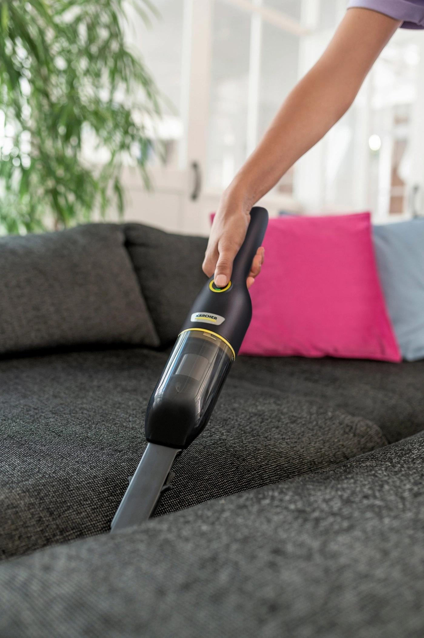 Eine Hand hält einen Handstaubsauger und reinigt ein Sofa.