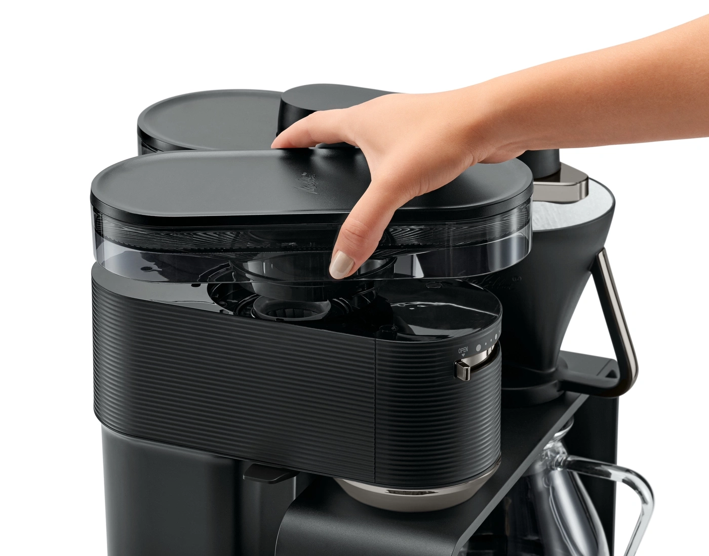 Eine Person öffnet den Deckel einer schwarzen Kaffeemaschine.