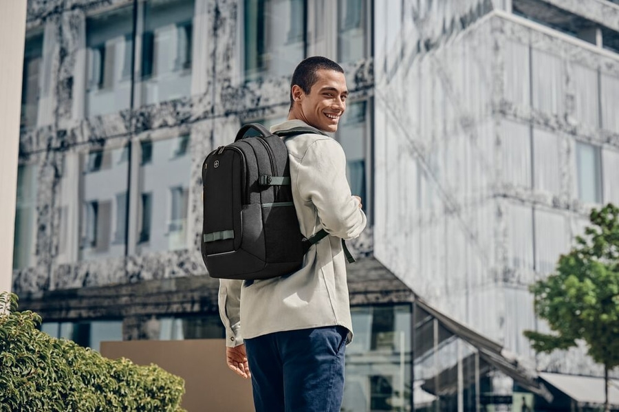 Mann mit Rucksack, der vor einem modernen Gebäude lächelt.