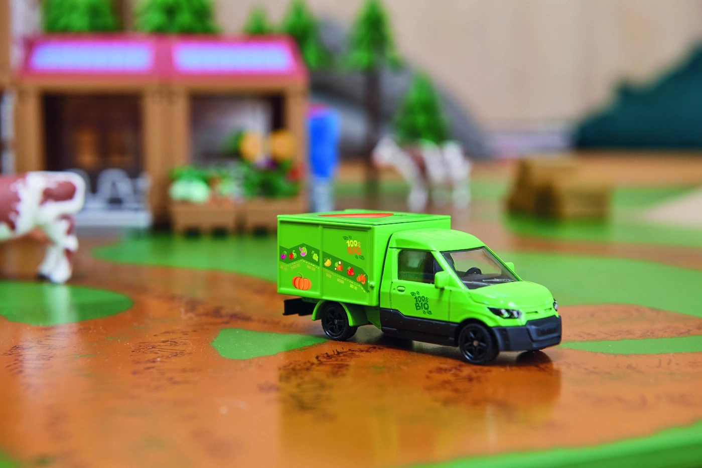 Grüner Spielzeug-Lieferwagen mit Bio-Gemüse-Aufdruck auf einem Bauernhof-Spielteppich.