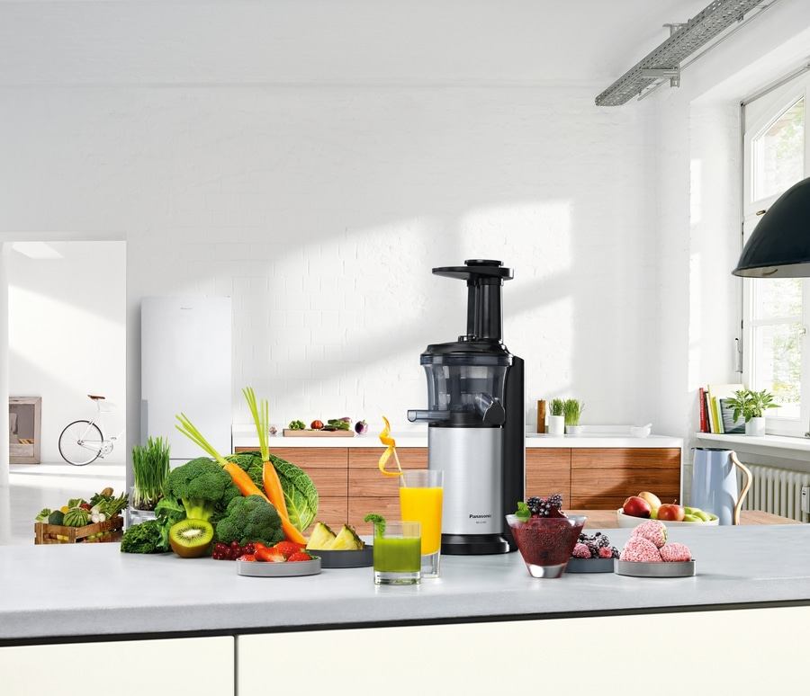 Küchenszene mit Entsafter, Gemüse, Obst und Getränken auf einer Arbeitsplatte