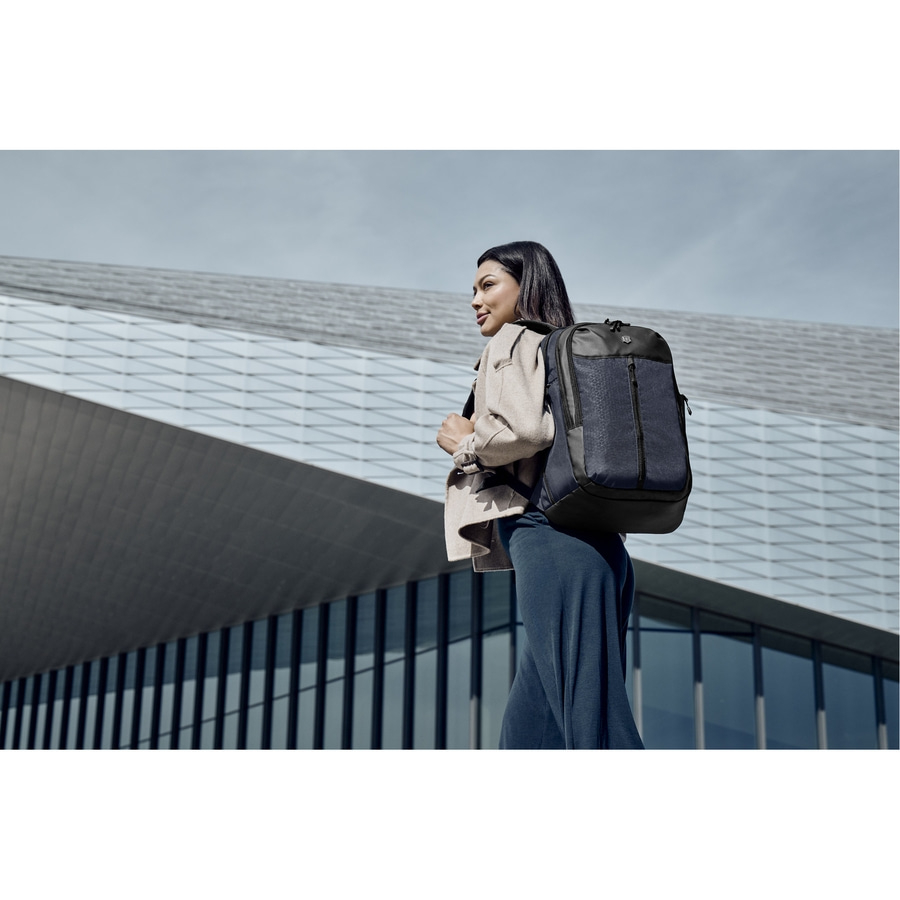 Eine Frau mit Rucksack vor einem modernen Gebäude. Sie schaut zur Seite.