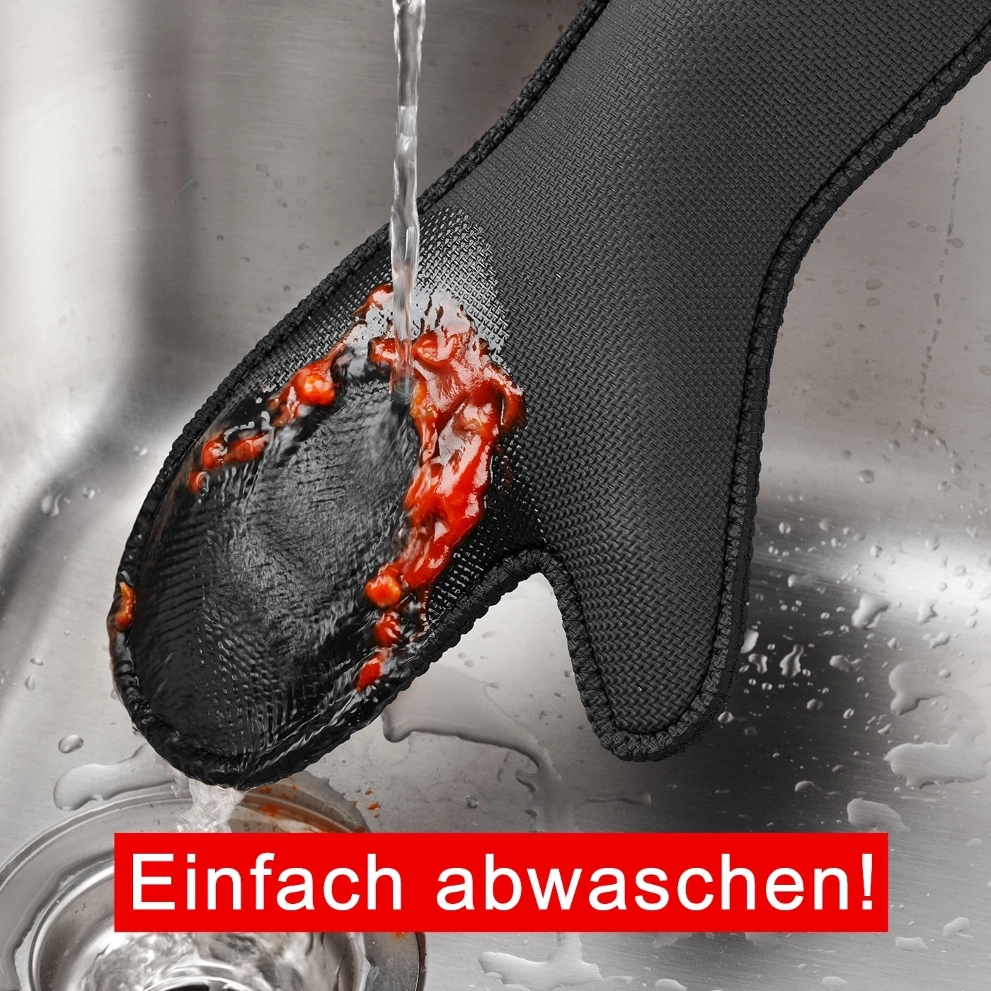 Schwarzer Topfhandschuh wird unter fließendem Wasser gereinigt, mit roter Sauce.