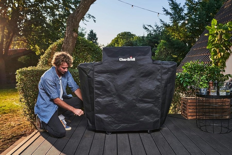 Mann kniet neben einem Grill, der mit einer schwarzen Abdeckung bedeckt ist.
