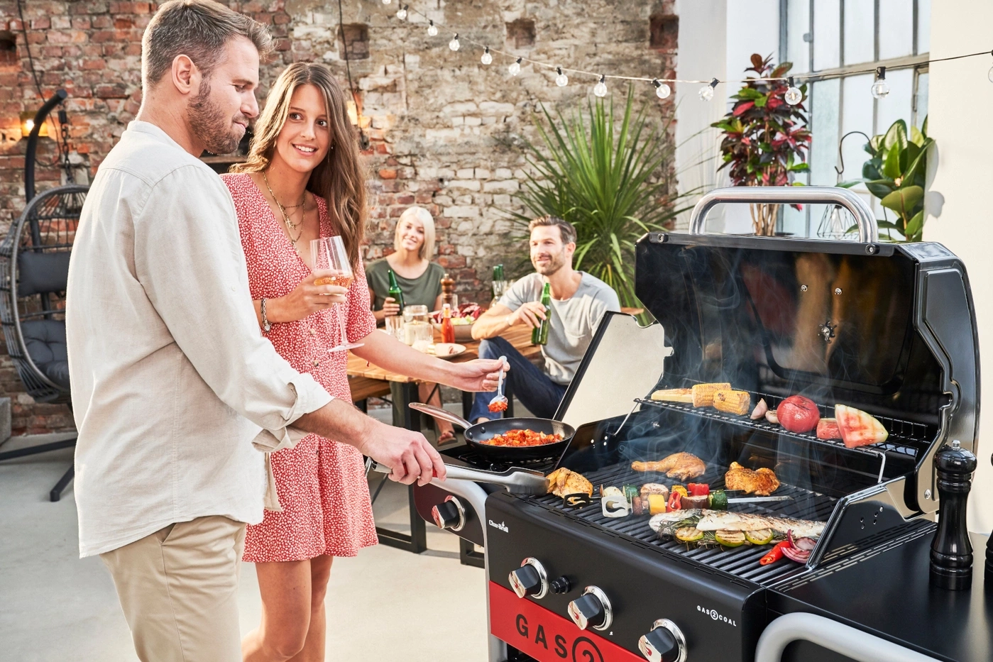 Ein Paar grillt bei einer Gartenparty, während Freunde im Hintergrund entspannen.