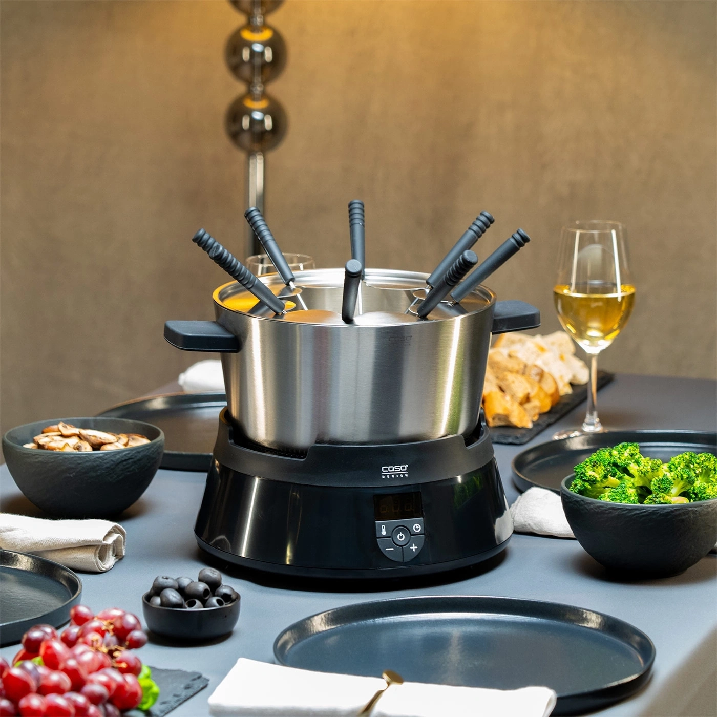 Käsefondue-Set mit Gemüse, Obst und Wein auf einem Tisch