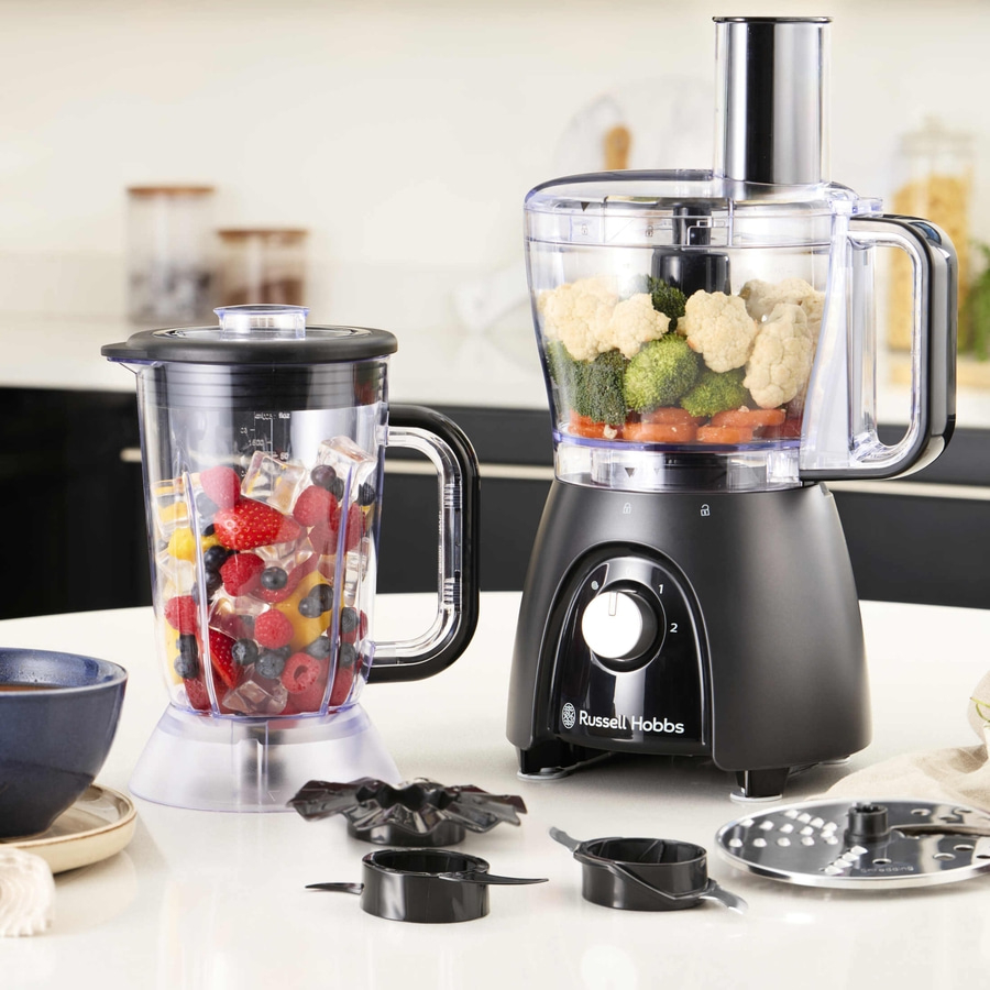 Küchengeräte: Mixer und Zerkleinerer mit Obst und Gemüse auf weißem Tisch