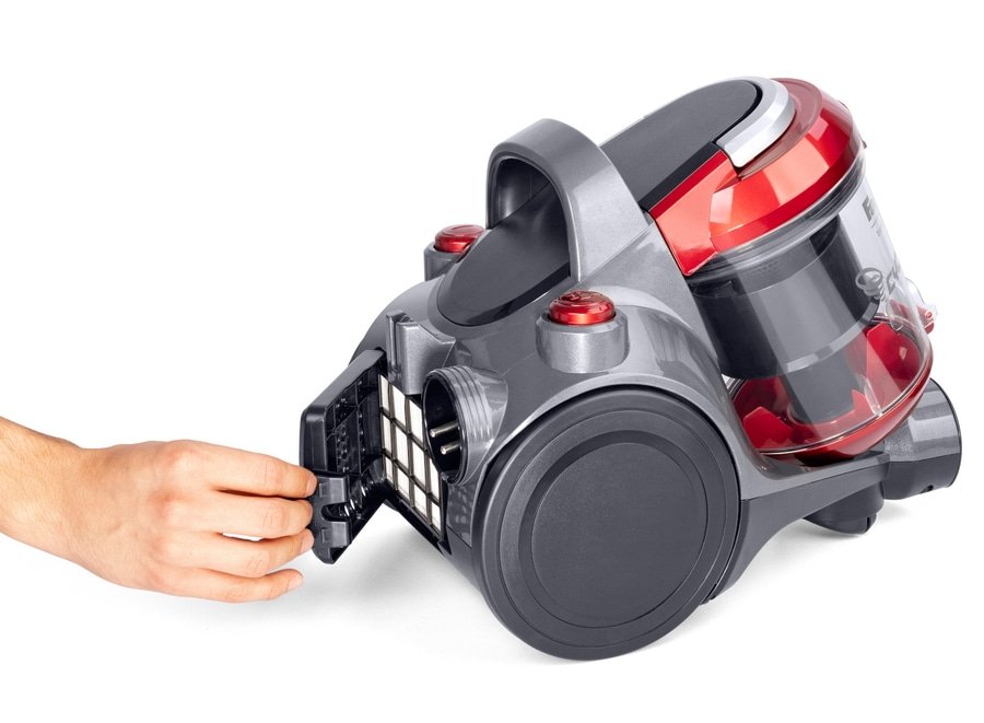 Ein Mann zieht einen Filter aus einem Staubsauger. Das Gerät ist grau und rot.